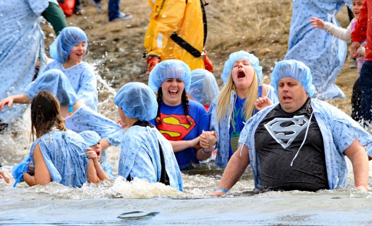 People wearing blue hospital gowns and hairnets submerge themselves in icy water during a polar plunge event at Big Bear