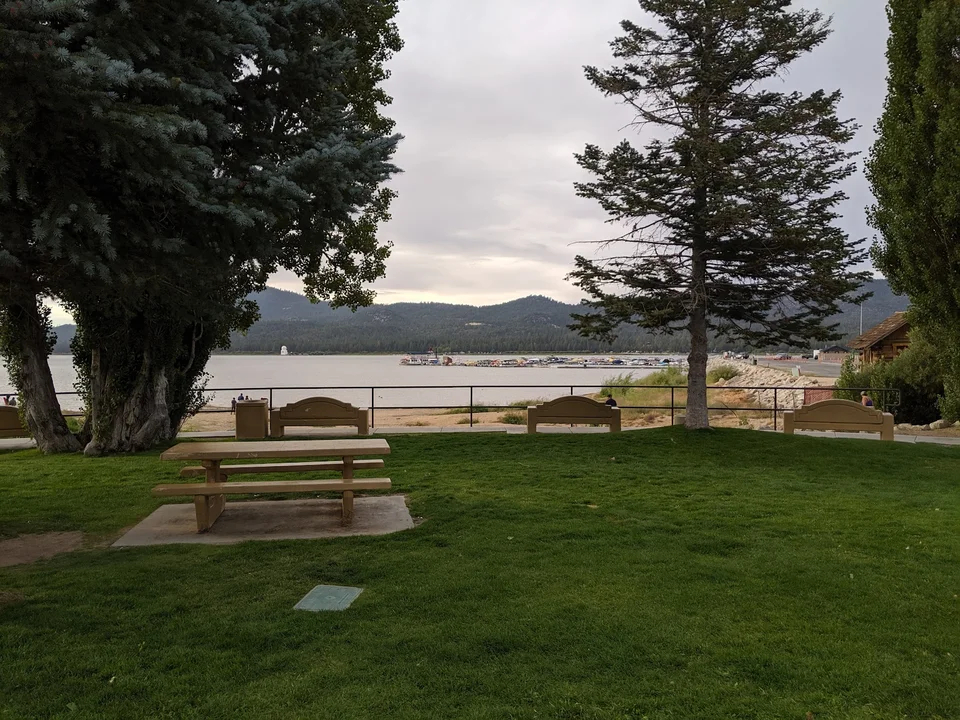 Lakefront lawn at Veterans Park in Big Bear featuring picnic tables, benches, mature trees, and views of Big Bear Lake.