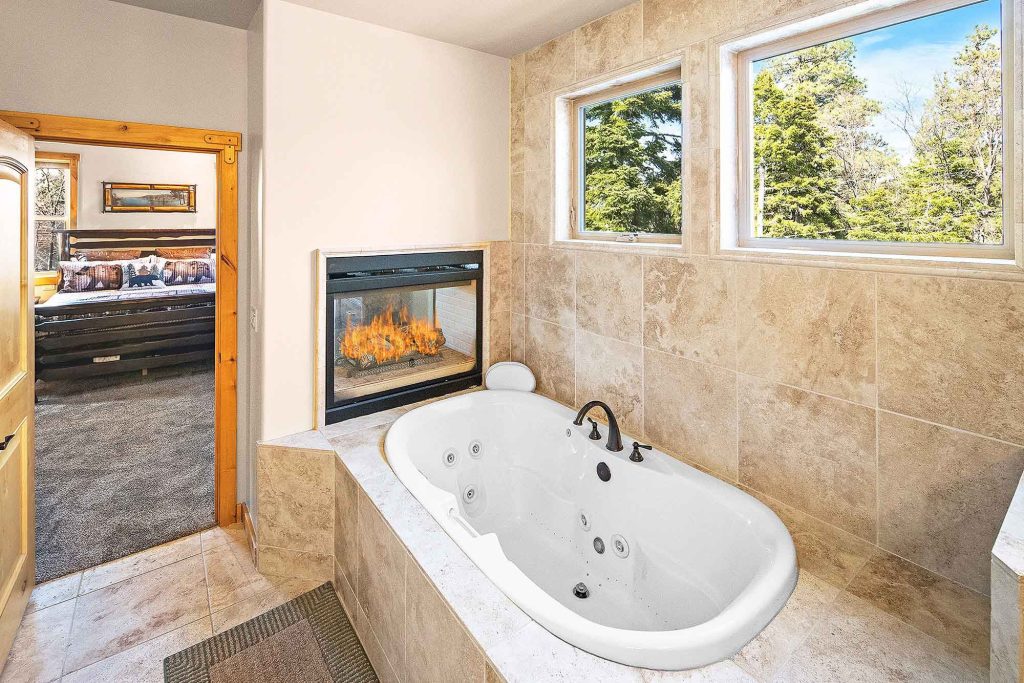 Luxury bathroom at Ridgecrest Lodge featuring a jacuzzi tub, fireplace, and forest view windows in Big Bear.