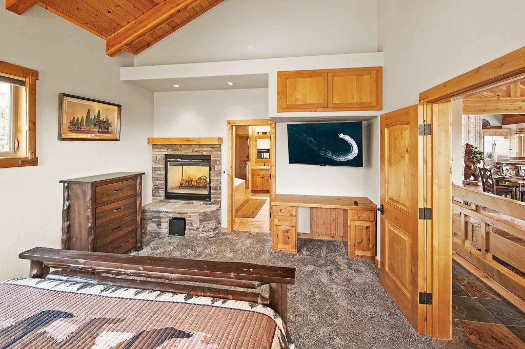 Cozy master bedroom at Ridgecrest Lodge with a stone fireplace, wood ceiling, and rustic mountain decor.