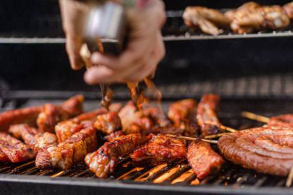 Grilled chicken and meat cooking on a barbecue grill with a chef adding seasoning for a flavorful outdoor meal