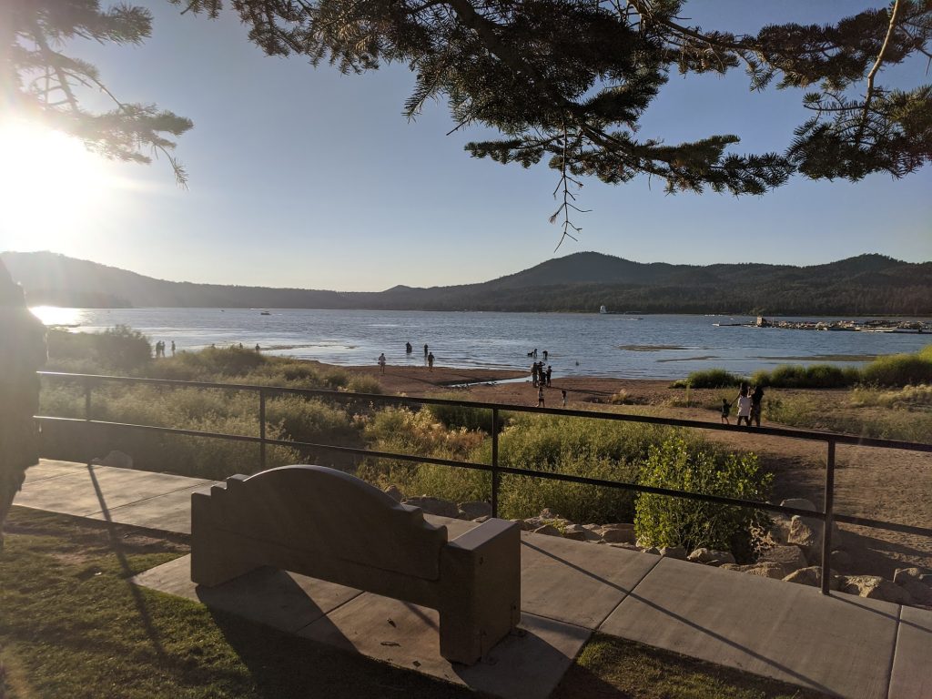 Scenic view of Rotary Pine Knot Park at Big Bear Lake with a pier, lakefront, and surrounding trees and mountains.
