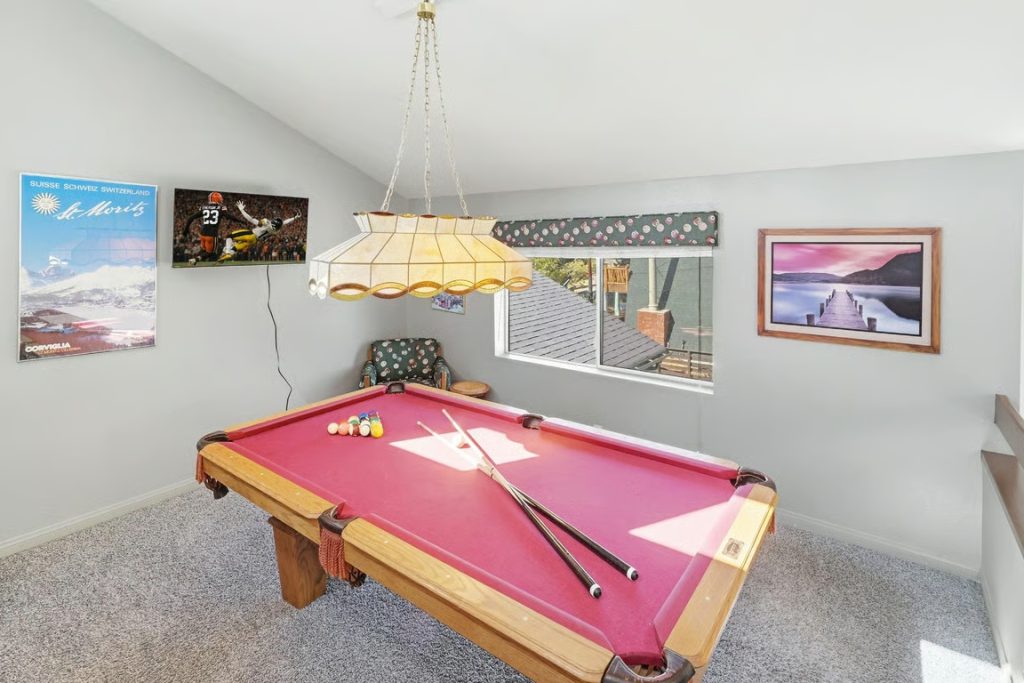Sandoval Slopes cabin game room in Big Bear featuring a red pool table, billiard cues, comfortable seating, and mountain-themed wall decor.