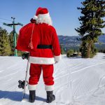 Photo of Santa Claus holding a snow board and looking down a ski run at Snow summit in big bear