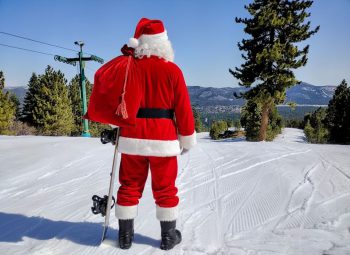 Photo of Santa Claus holding a snow board and looking down a ski run at Snow summit in big bear