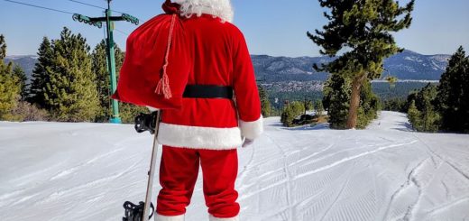 Photo of Santa Claus holding a snow board and looking down a ski run at Snow summit in big bear