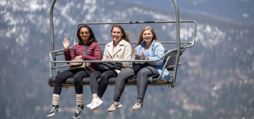 Three girls sitting on a ski lift, enjoying the snowy views of Big Bear Lake in the background.