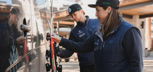 A man an a woman in winter coats with blue hats on and carrying skis at the back of a van.