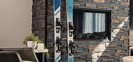 Two pairs of skis and ski boots leaned against a fireplace during the day inside a home.