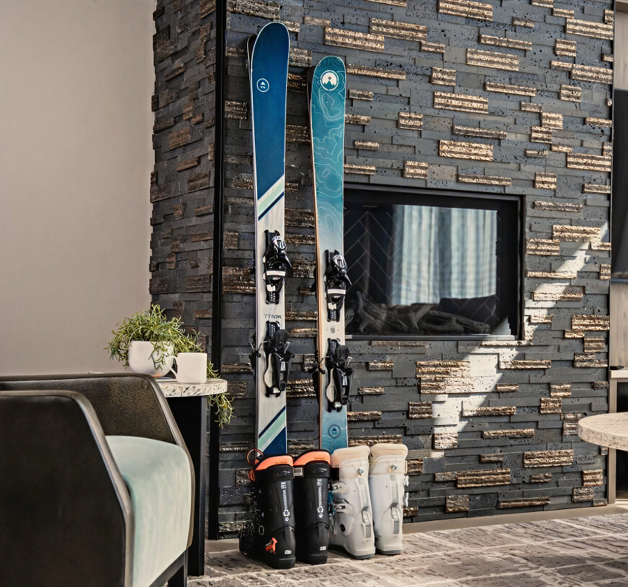 Two pairs of skis and ski boots leaned against a fireplace during the day inside a home.
