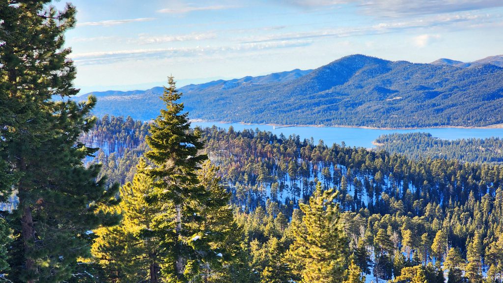 A beautiful view of Big Bear Lake and the surrounding snow-covered mountains, with evergreen trees in the foreground.