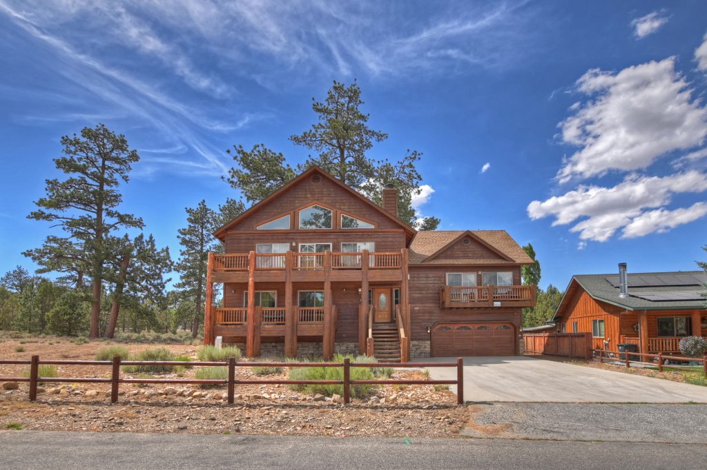 A beautiful two-story wooden cabin with a deck and a garage sits under a bright blue sky in Big Bear.