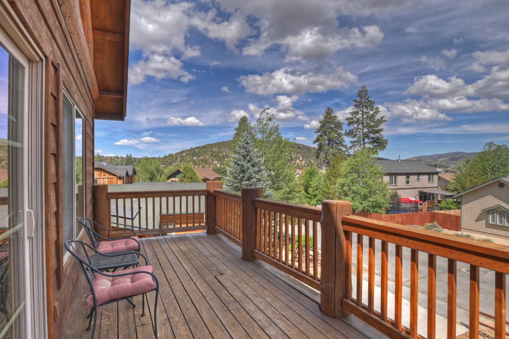 A wooden deck with two chairs offers a view of a residential area and a hillside in Big Bear.