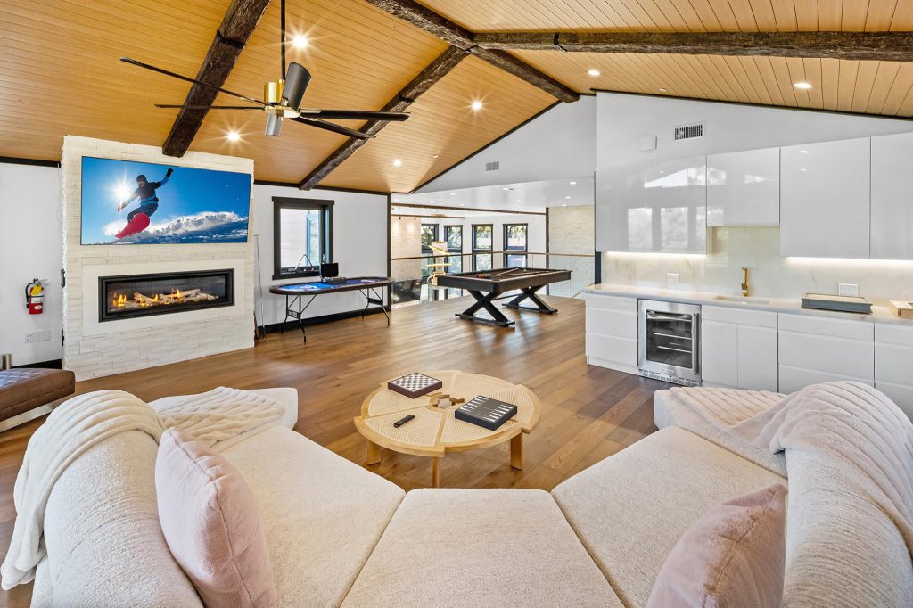 A modern cabin living room in Big Bear with a white sectional sofa, a fireplace, and a bar area with a pool table.
