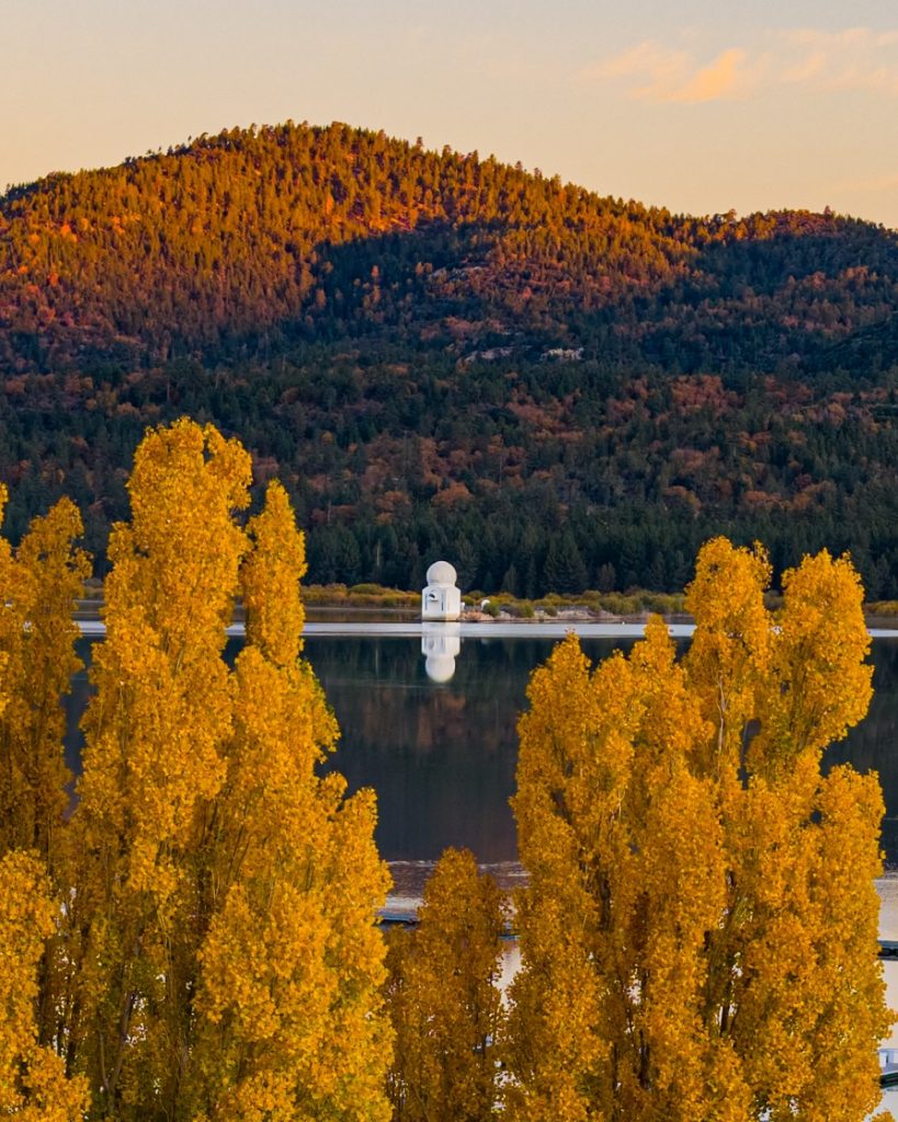 Scenic Big Bear Lake landscape with golden autumn trees, calm water, and forest-covered mountains in the background