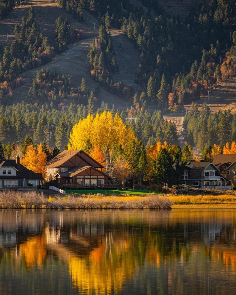 Scenic Big Bear Lake view with golden autumn trees, mountain landscape, and cabin homes reflecting on calm water