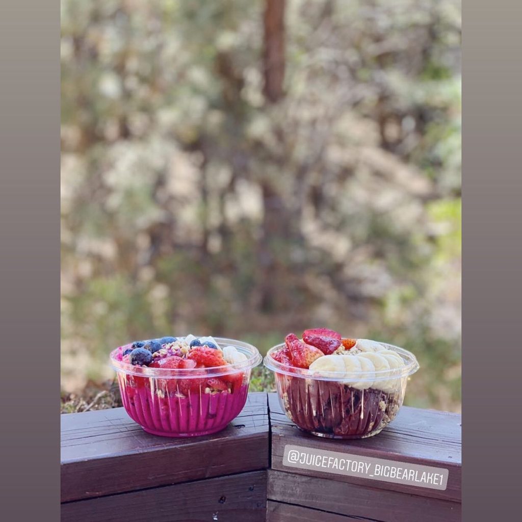 Fresh acai bowls from Juice Factory Big Bear served outdoors with fruit toppings and a scenic forest background.