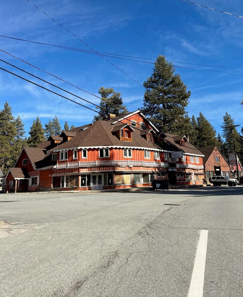 Historic mountain lodge building with rustic wooden architecture surrounded by pine trees under a blue sky.