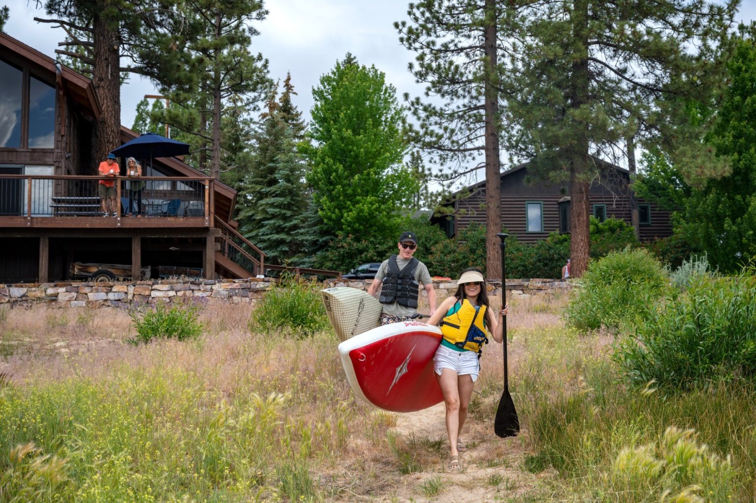 Visitors enjoying kayaking and paddleboarding near a Big Bear Lake cabin surrounded by trees and mountain scenery
