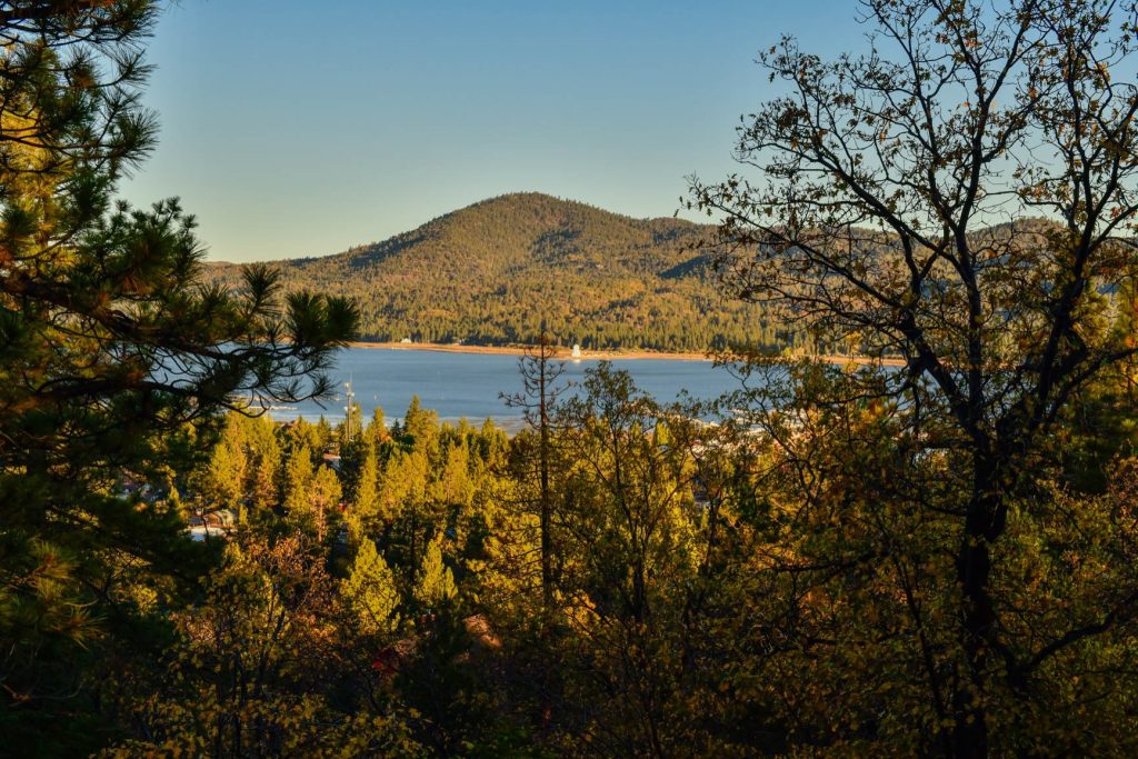 Scenic mountain lake view surrounded by pine trees and forest landscape under a clear sky.