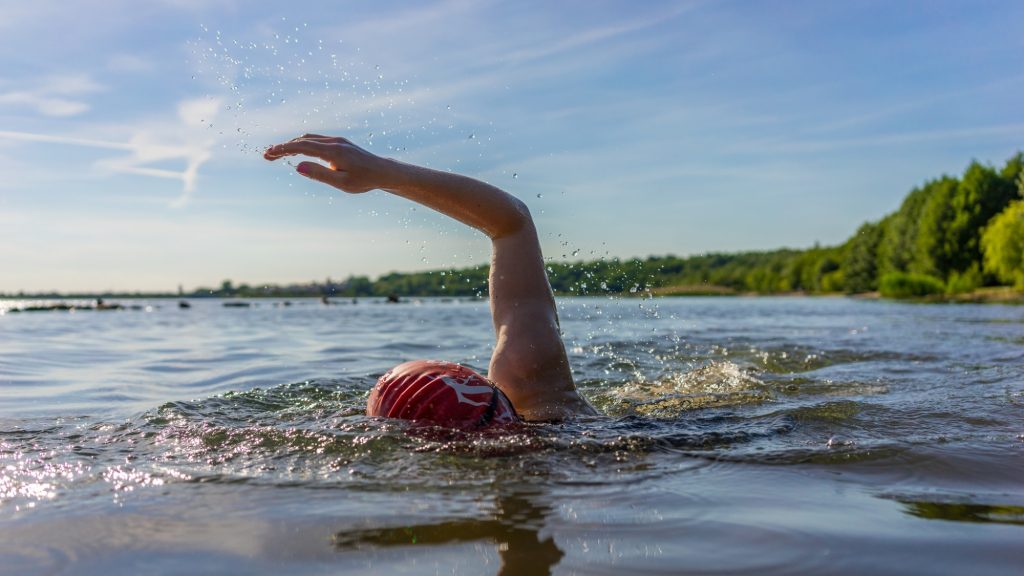 Person swimming in a lake with water splashing under a clear blue sky.