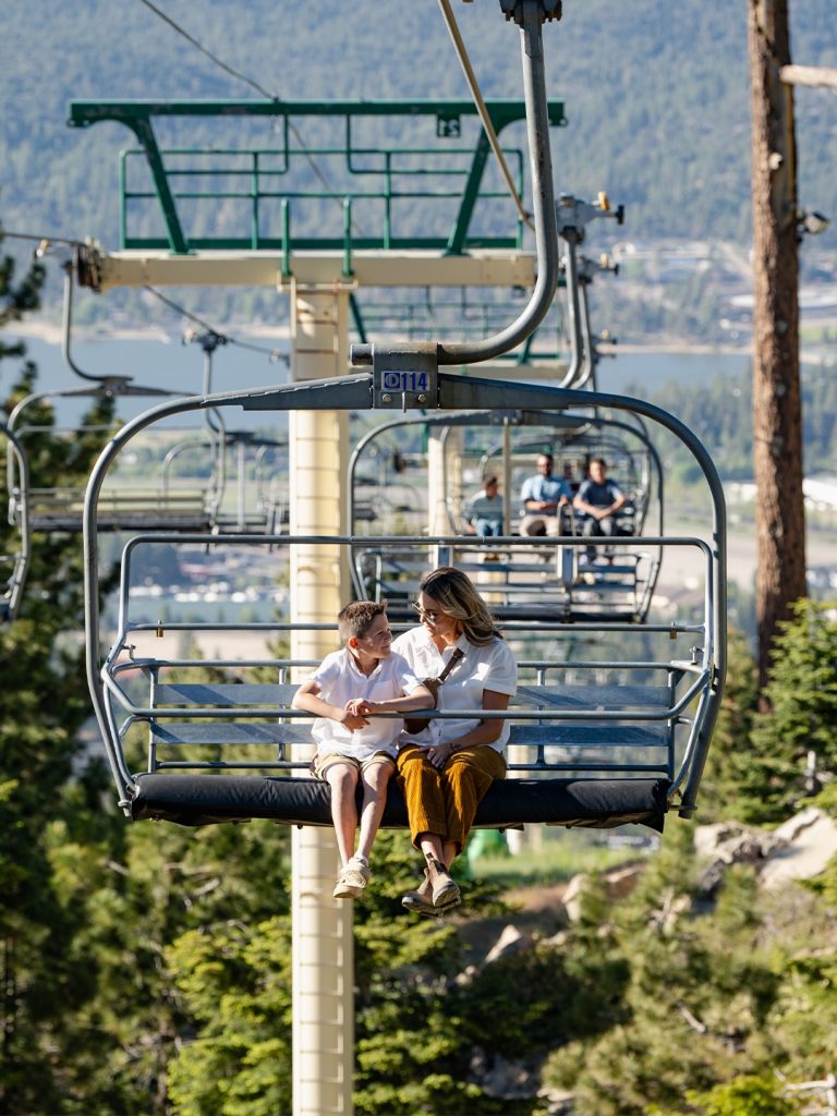 Parent and child enjoying a scenic chairlift ride overlooking Big Bear Lake and the surrounding mountains.