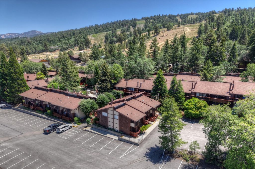 Aerial view of Snow Summit mountain resort area with cabins, parking lots, and forested hillside surrounding the slopes