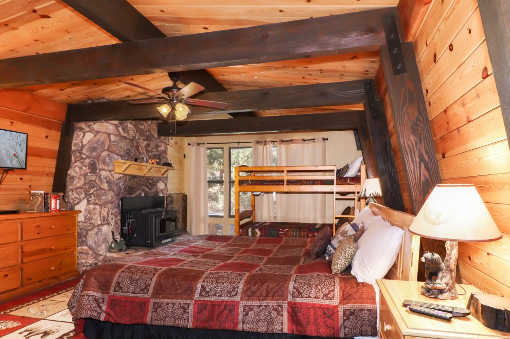 Rustic bedroom with wood beam ceiling, stone fireplace, and bunk bed