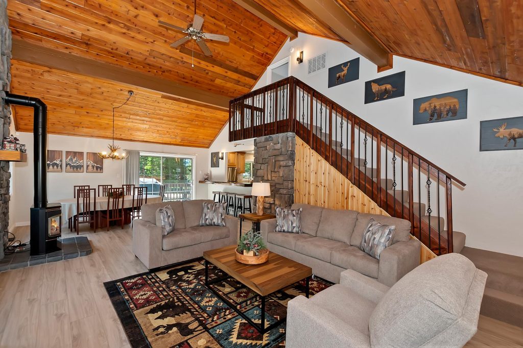 Spacious living room with vaulted wood ceilings, stone fireplace, staircase, and dining area