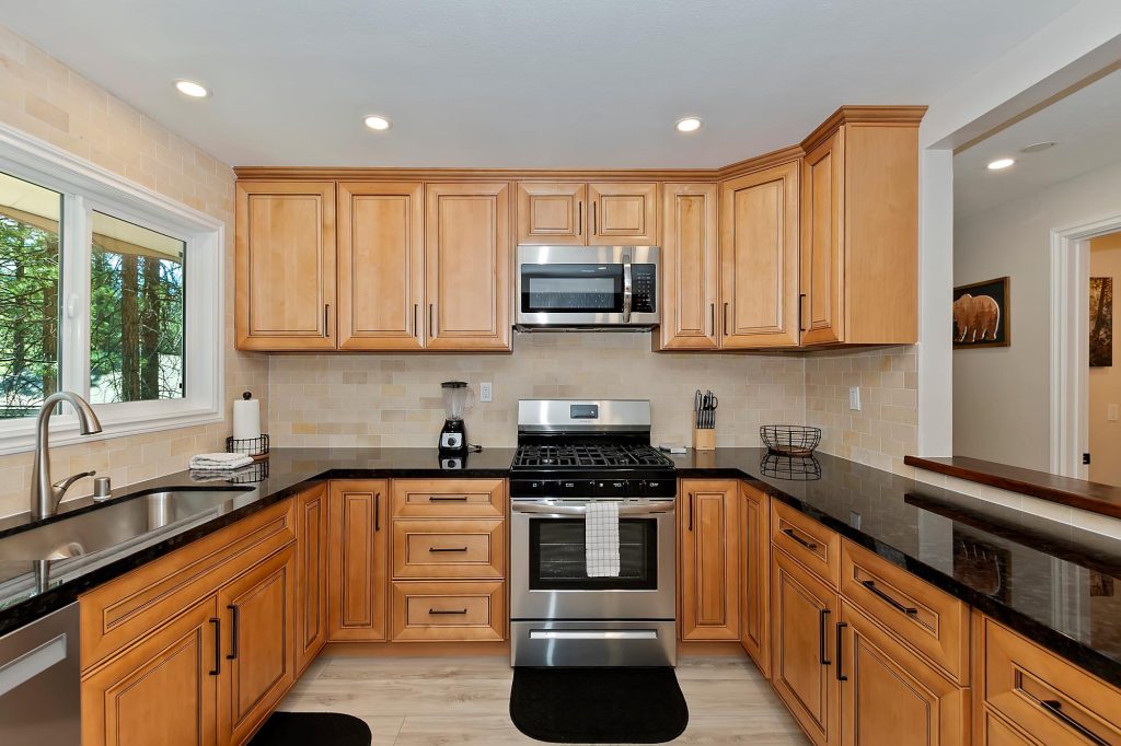 Modern kitchen with light wood cabinetry, black countertops, and stainless steel appliances