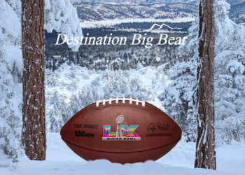 A football with Super Bowl LX logo on the front set in between two pine trees and a snowy mountain background behind