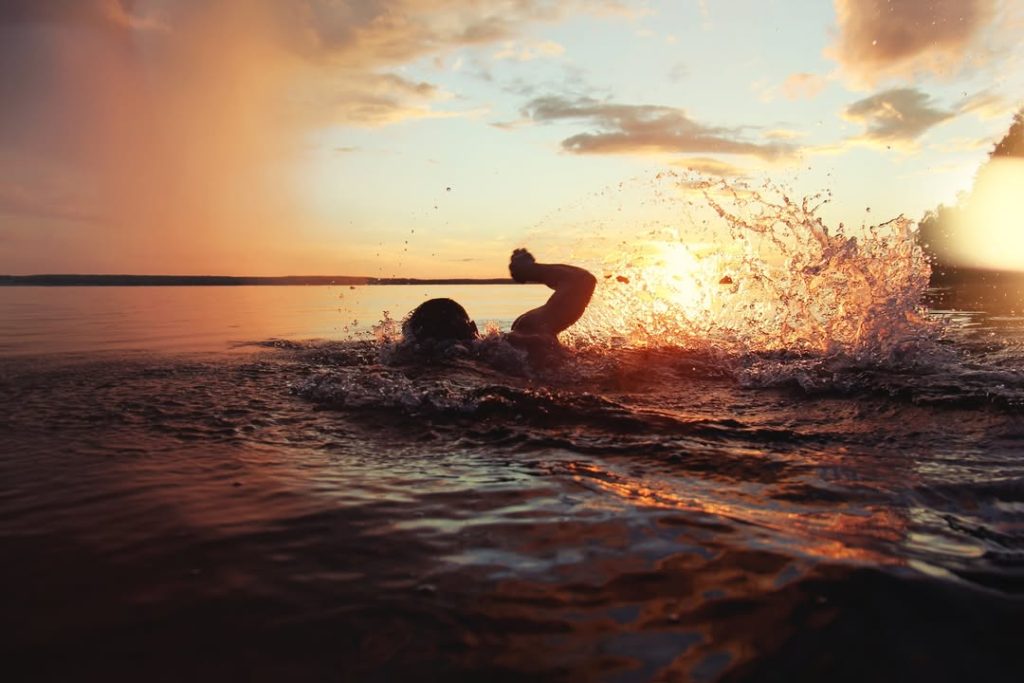 A swimmer in open water splashing vigorously during sunset, with golden light reflecting across the lake and dramatic water droplets in the air.