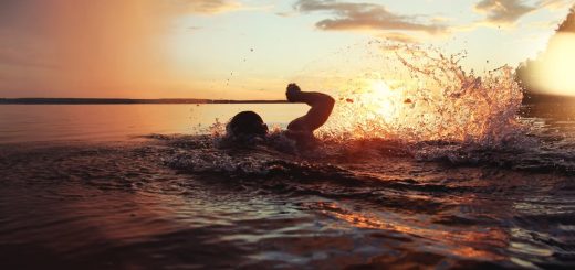 A swimmer in open water splashing vigorously during sunset, with golden light reflecting across the lake and dramatic water droplets in the air.