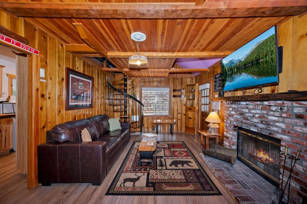 Rustic living room at The Cuddly Bear Cabin featuring a brick fireplace, leather sofa, wood interior, and cozy mountain cabin decor