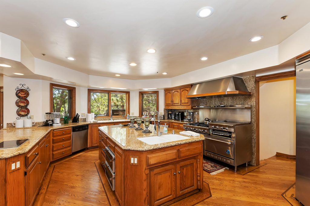 Spacious mansion kitchen featuring wooden cabinetry, granite countertops, large island, premium appliances, and modern cooking space