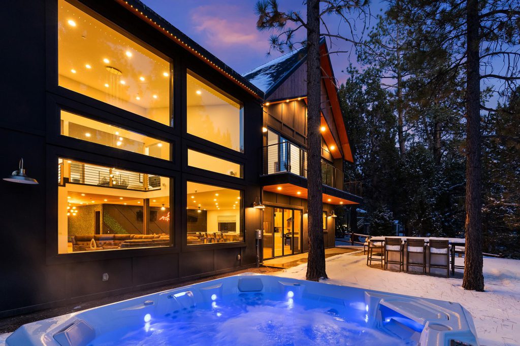 A modern-looking cabin with wood and dark siding, lit up at dusk in Big Bear.