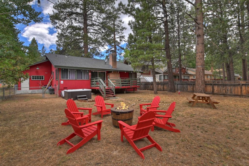 Backyard of The Ginger Lodge featuring red Adirondack chairs around a fire pit with a deck and hot tub
