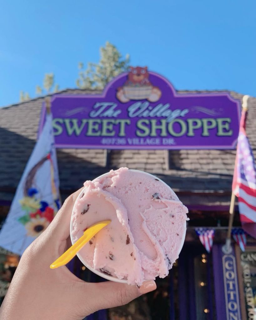 Hand holding a cup of pink ice cream in front of The Village Sweet Shoppe in Big Bear Lake.