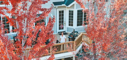 The Hidden Estate – person standing on the deck of the house surrounded by red autumn trees