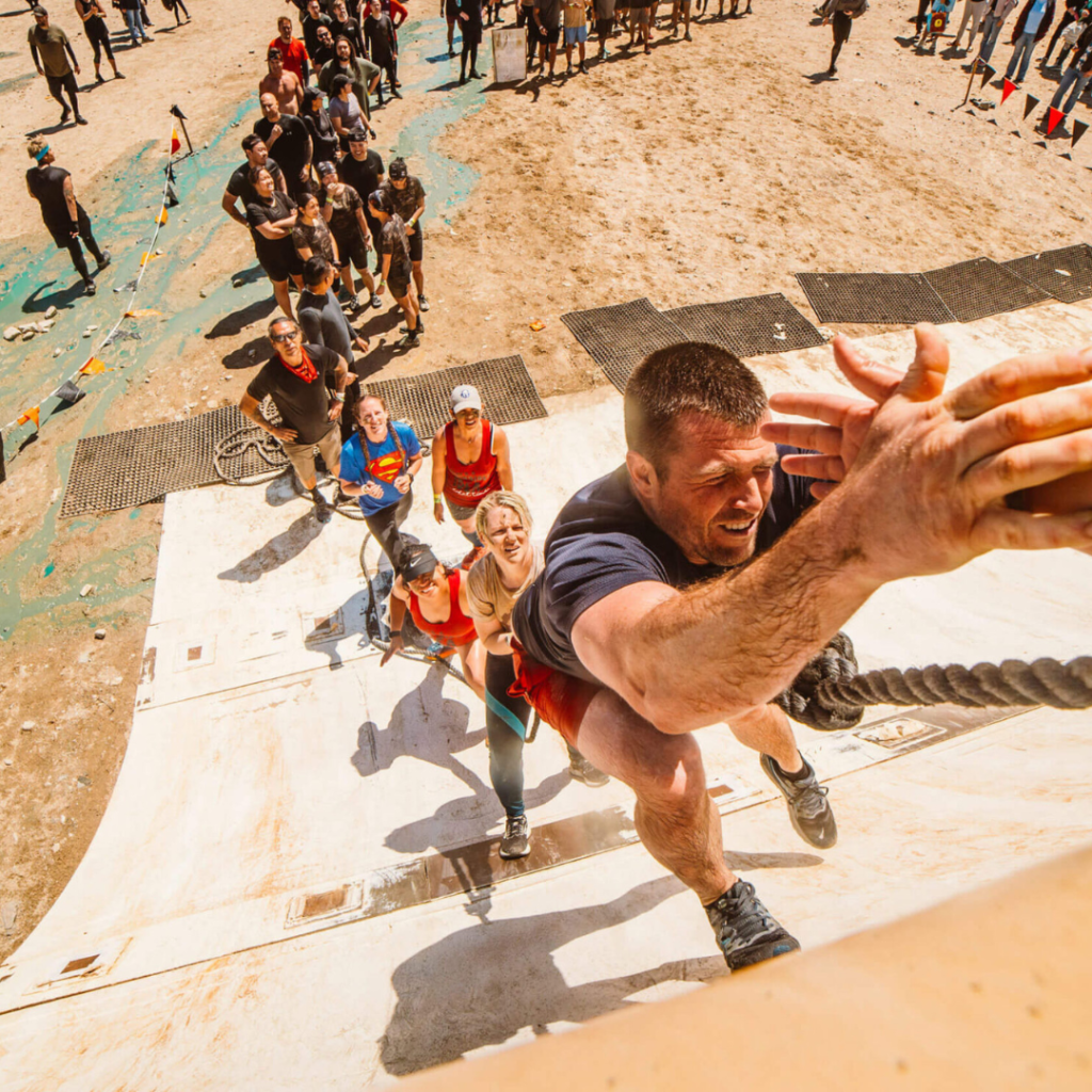 Participants climbing an obstacle with ropes at a Tough Mudder event, viewed from above