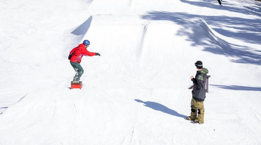 Two snowboarders stand at the top of a snowy slope in Big Bear Lake, ready to descend the hill.