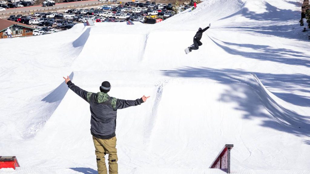 Two snowboarders stand at the top of a snowy slope in Big Bear Lake, ready to descend the hill.