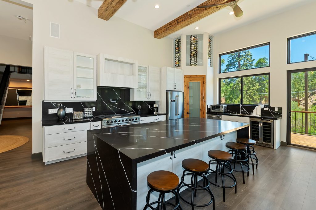 A modern kitchen in a Big Bear home with white cabinets, a large black marble island with bar stools, and a built-in wine rack.