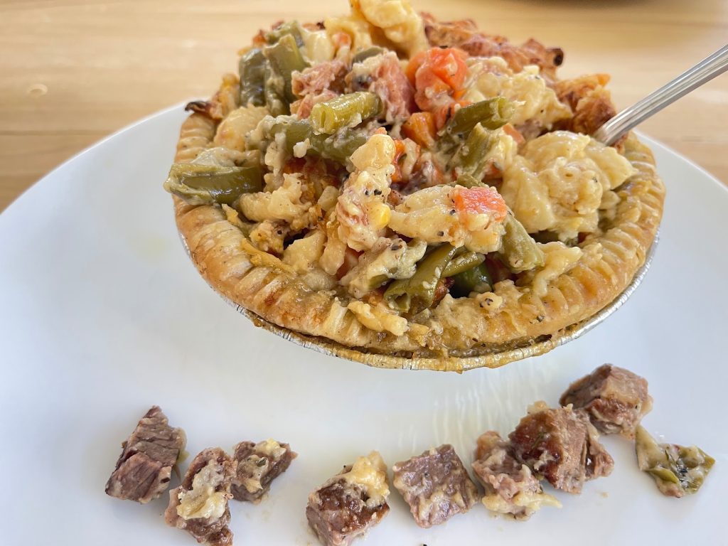 Close-up of a vegetable and cheese pot pie in a golden crust with chunks of green beans, carrots, and macaroni.