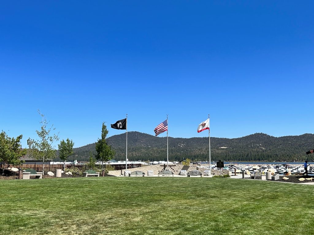 Memorial flag display at Veterans Park in Big Bear featuring American, California, and POW/MIA flags with Big Bear Lake and mountain scenery in the background.