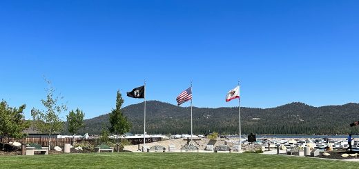 Memorial flag display at Veterans Park in Big Bear featuring American, California, and POW/MIA flags with Big Bear Lake and mountain scenery in the background.