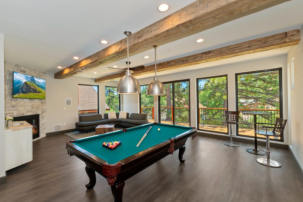 A modern Big Bear living area with a billiards table, fireplace, and large windows looking out to a deck.