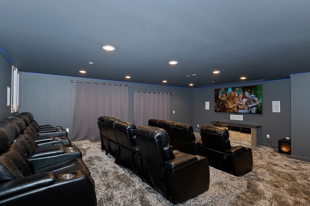 A modern home theater in Big Bear with two rows of black leather seats, a large television on a mirrored stand, and a gray, shaggy carpet.
