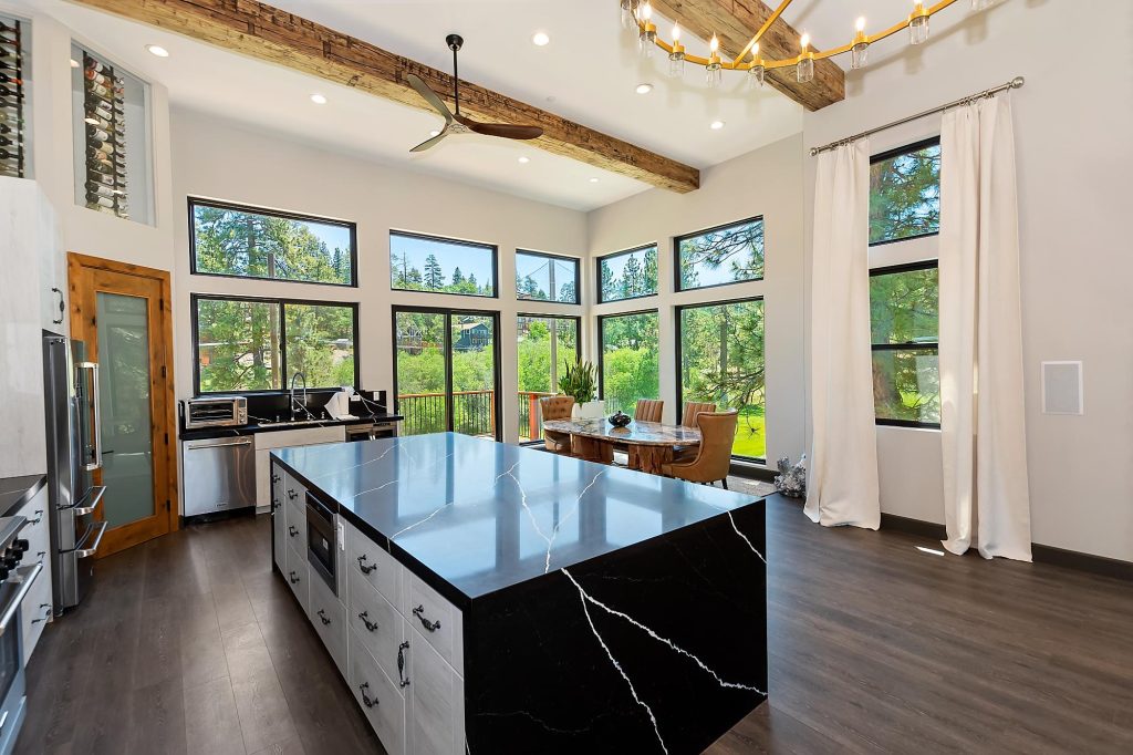 Modern kitchen with black island countertop, large windows, and forest views