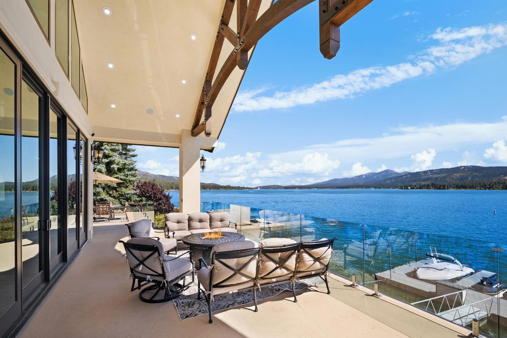A modern patio with outdoor seating and a glass railing overlooks Big Bear Lake and a boat dock.